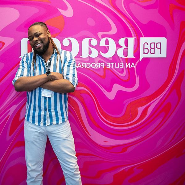 Man posing in front of a pink Beacon branded sign with a blue stripped shirt