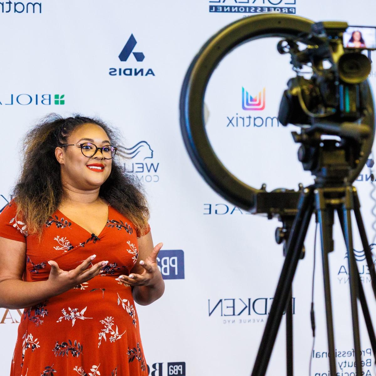 Image of a woman in a red dress in front of a camera